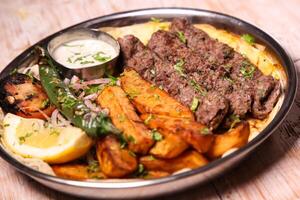 Kebab Laham or lamb kabab with salad, wedges, lemon and dip served in dish isolated on background top view of arabic food photo