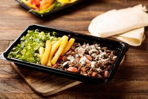 Beef Shawarma plate with salad, fries and pita bread served in a dish isolated on wooden table background side view of fastfood photo