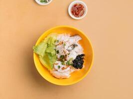 Thai food Sliced Fish Porridge in a bowl with soup, chili sauce and spring onion top view on wooden table photo