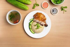 Roasted Chicken and Roast Pork Rice with raw cucumber, Coriander, salad, sauce and soup served in a dish isolated on wooden background top view photo