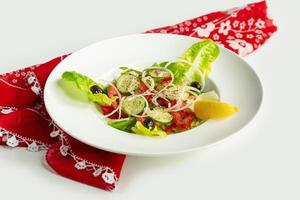 Fresco sano verde ensalada en un plato aislado en vistoso mesa paño parte superior ver en gris antecedentes tomate, pepino, cebolla, espinaca, lechuga y sésamo foto