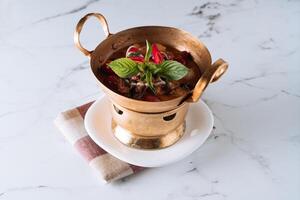 Lychee Roasted Duck Curry in a copper stew dish isolated on mat top view on grey marble background photo