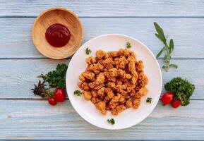 Homemade Crispy Popcorn Chicken in white plate with tomato ketchup and bbq sauce isolated on wooden table background top view fast food photo