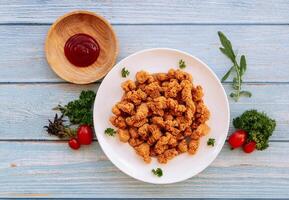 hecho en casa crujiente palomitas de maiz pollo en blanco plato con tomate salsa de tomate y barbacoa salsa aislado en de madera mesa antecedentes parte superior ver rápido comida foto