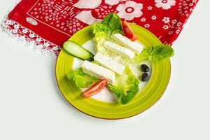 Traditional Turkish Cheese or Beyaz Peynir with cucumber and tomato in a dish isolated on colorful table cloth top view on grey background photo