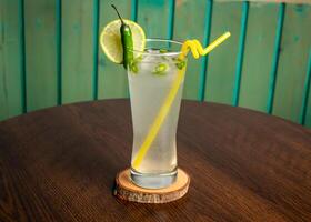 refreshing glass of Spicy Lemonade with lime slice, green chili and straw isolated on wooden table side view ramdan drink photo