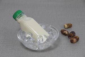 A bottle of Dates Milk served in iced cube bowl side view on grey background photo