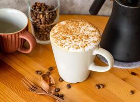 Cappuccino with cinnamon powder, coffee beans, fork, spoon served in cup isolated on wooden table top view of taiwan food photo