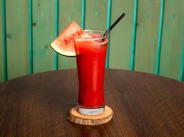 A glass of watermelon juice shake with raw watermelon, straw isolated on wooden table side view healthy drink for vitamin c photo