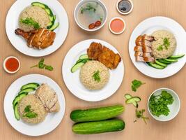 Chicken Cutlet and Roast Pork Rice, Roast Pork, Roasted Chicken, Roast Pork, Steamed Chicken with raw cucumber, Coriander, salad, sauce and soup served in a dish isolated on wooden background top view photo