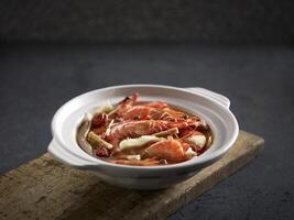 Poached Tiger Prawns with Superior Stock and Chinese Herbs served in a pot isolated on cutting board side view on dark background photo