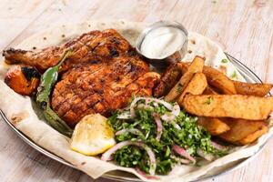 Half grilled chicken with salad, wedges, lemon and dip served in dish isolated on background top view of arabic food photo