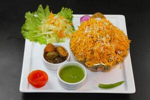 Chicken biryani with salad, raita, mint chutney and pickle served in a karahi isolated on dark background side view of indian spicy food photo