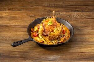 Red Curry Duck Confit with Crispy Noodles served in a pan top view on dark wooden background photo