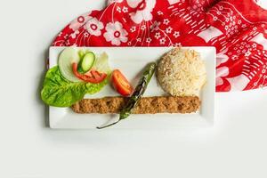 Turkish style adana kebab with rice and salad in a dish isolated on colorful table cloth top view on grey background photo