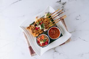 Traditional Malaysian food chicken satay skewers with chili sauce and salad in a dish isolated on mat top view on grey marble background photo