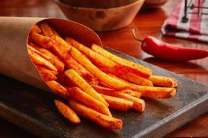 Spicy french Fries served in a wooden board isolated on wooden background side view photo
