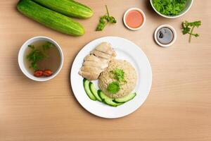 Steamed Chicken Rice with raw cucumber, Coriander, salad, sauce and soup served in a dish isolated on wooden background top view photo