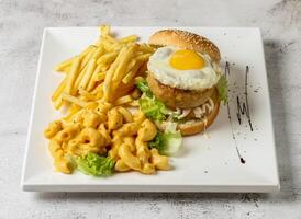 clásico Cerdo hamburguesa con soleado lado arriba huevo, Mac y queso y francés papas fritas servido en plato aislado gris antecedentes parte superior ver Singapur rápido comida foto