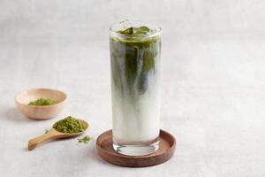 vaso de con hielo matcha latté, verde té con Leche y soja leche. azotado matcha té con matcha polvo cuchara aislado en gris antecedentes. foto