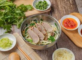 Duck meat rice noodles soup with chilli sauce, noodles, spoon and chopsticks served in dish isolated on napkin top view of hong kong food photo