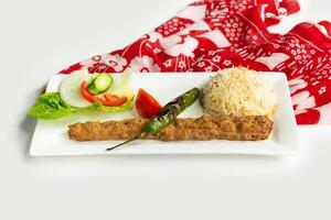 Turkish style adana kebab with rice and salad in a dish isolated on colorful table cloth side view on grey background photo