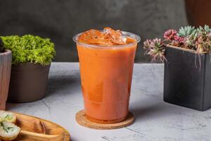 Thai milk tea served in disposable glass with ice cube isolated on wooden board side view of taiwanese ice drink photo