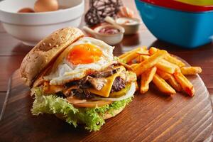 Mushroom Swiss beef burger with sunny egg and fries served in a dish isolated on wooden background side view photo