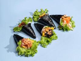 Assorted japanese wraps Spicy TAMAGO, CALIFORNIA wrap, POKE SALMON Skin, SPICY TUNA roll topping with salad leaves isolated on sky blue background side view fast food photo