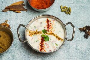 Chatpati Mixed Raita with cucumber, onion, masala and dahi or yogurt served in a dish isolated on grey background top view of bangladesh food photo