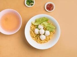 delicious thai food Fishball Noodle in a bowl with soup, chili sauce and spring onion top view on wooden table photo
