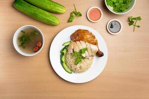 Steamed and Roasted Chicken Rice with raw cucumber, Coriander, salad, sauce and soup served in a dish isolated on wooden background top view photo