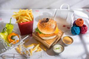 Fish Burger with fries tomato, and green chilli isolated on wooden board side view of american fast food photo