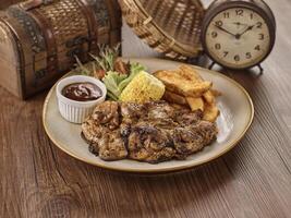 Grilled Chicken Chop, chips and corn in a dish isolated on dark wooden table side view singapore food photo