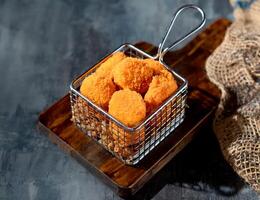 Golden Scallops in a deep fryer dish on wooden board side view on dark background photo