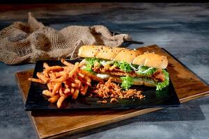 Crispy Fish Burger with fries in a black dish on cutting board side view on dark background fast food photo
