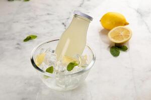 un botella de sano limón y menta jugo servido en con hielo cubo cuenco lado ver en gris antecedentes foto