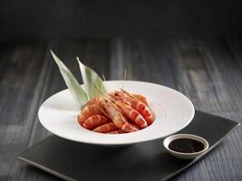 Poached Tiger Prawns served in a pot isolated on cutting board side view on dark background photo