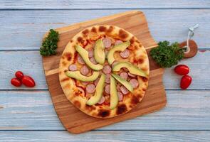 Smokey Sausage Avocado Pizza with tomato on wood table background top view photo