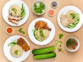 Chicken Cutlet and Roast Pork Rice, Roast Pork, Roasted Chicken, Roast Pork, Steamed Chicken with raw cucumber, Coriander, salad, sauce and soup served in a dish isolated on wooden background top view photo