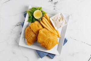 Fried Fish and Chips with lime in a dish basket isolated on napkin side view on grey background famous indian and pakistani food photo