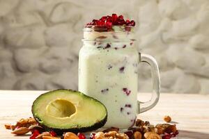 avocado milkshake with nuts, pomegranate seeds, walnut, almond and cashew served in jar isolated on background top view of healthy morning drink photo