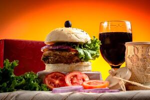 Traditional Beef burger with cold drink, tomato slice isolated on wooden board side view on table fast food photo