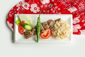 Turkish barbecues Sis lamb Kebab with rice and salad in a dish isolated on colorful table cloth top view on grey background photo
