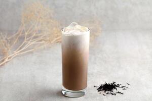 Glass of iced milk tea with ice cubes on grey background photo