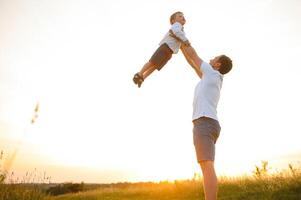 joven padre lanza arriba su linda y pequeño hijo en el Fresco aire. del padre día, padre y su hijo bebé chico jugando y abrazando al aire libre. foto