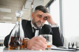 Old male employee drinking alcohol at workplace photo