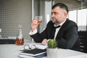 Old male employee drinking alcohol at workplace photo