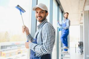 Young indian man washing window in office. photo