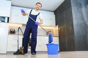 profesional limpiador en azul uniforme Lavado piso y limpiando polvo desde el mueble en el vivo habitación de el departamento. limpieza Servicio concepto foto